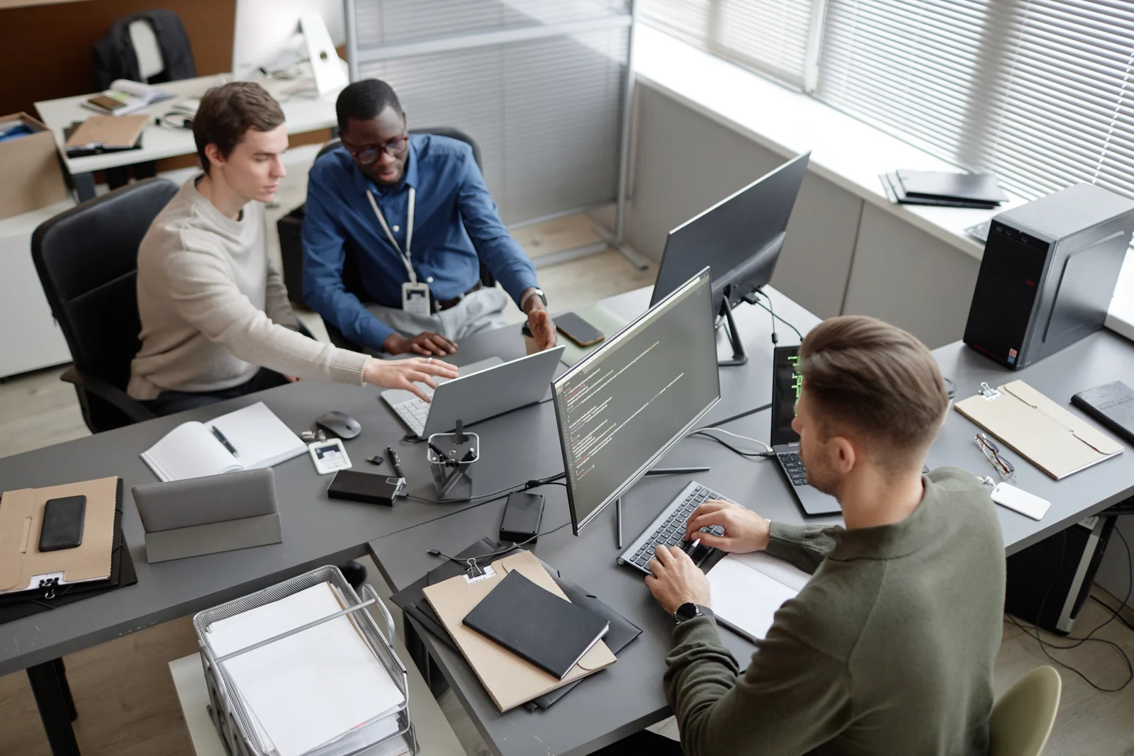 Three IT professionals working together at computers in a bright office.