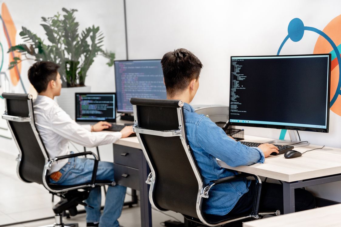Two professionals working at screens displaying code in a bright office.